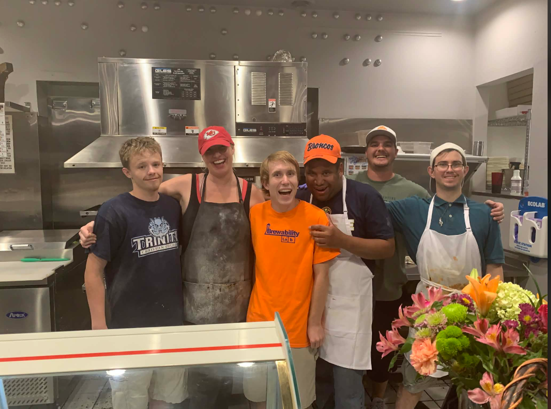 Six Pizzability crew members smiling together in the restaurant kitchen.